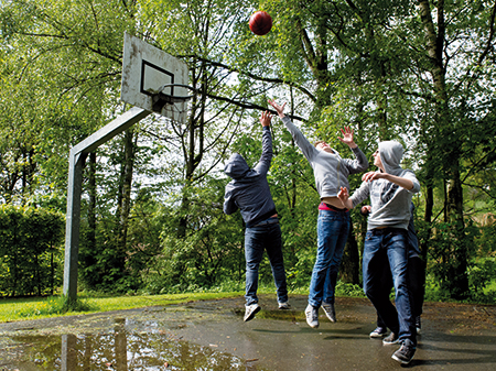 Drei Jugendliche spielen draußen Basketball.