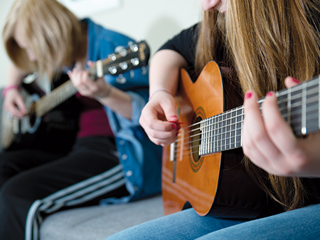 Zwei Mädchen sitzen nebeneinander und üben Gitarre spielen.